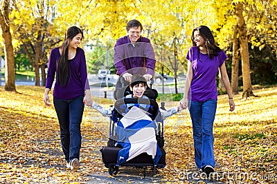 Family with disabled child in wheelchair walking among autumn le Stock Photo