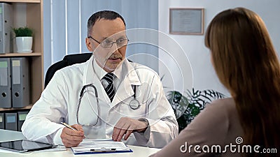 Family doctor listening to patient, filling out medical insurance, health care Stock Photo