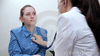 Family doctor therapist listens to heart and lungs with stethoscope of girl patient in office. Young woman at doctor& x27;s Stock Photo