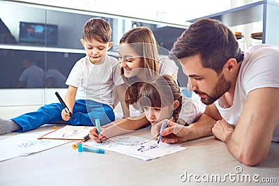 A family draws on paper lying on their free time on the floor. Stock Photo