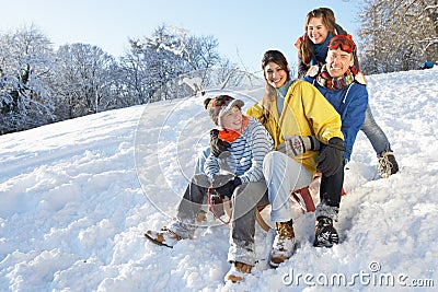 Family Enjoying Sledging Down Snowy Hill Stock Photo