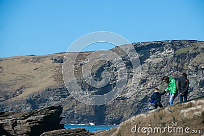 Family of father, mother, child with their backs to camera make their away across rocks to the ocean Editorial Stock Photo