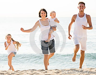 Family of four running on sandy beach on sunny weather Stock Photo