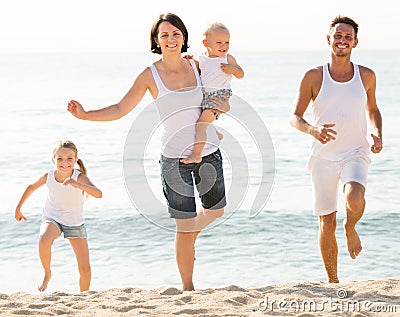 Family of four running on sandy beach on sunny weather Stock Photo