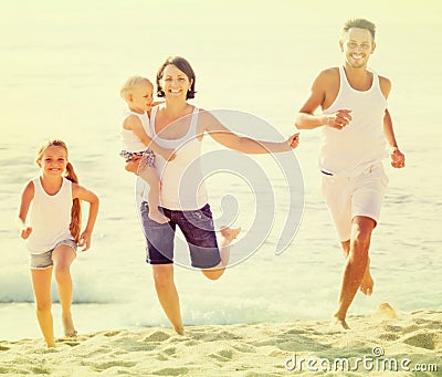 Family of four running on sandy beach on sunny weather Stock Photo