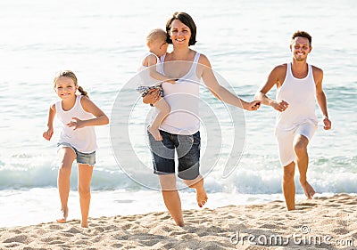 Family of four running on sandy beach on sunny weather Stock Photo