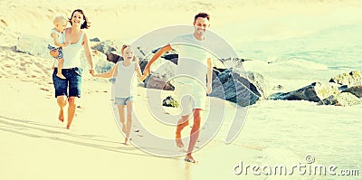 Family of four running on sandy beach on sunny weather Stock Photo