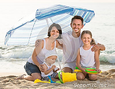 Family of four sitting together under beach umbrella on beach Stock Photo