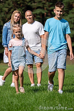 A family of four walks hand in hand through a sunny park, showcasing a moment of unity, bonding and peaceful coexistence Stock Photo