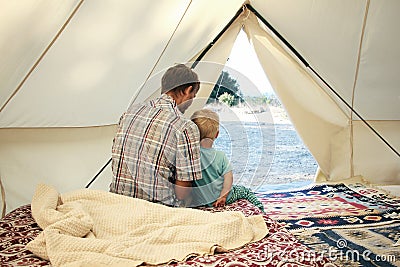 Family glamping. Father and his toddler son inside big camping tent with cozy interior. Luxury travel accomodation into the forest Stock Photo