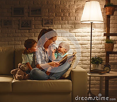 Family before going to bed mother reads children book about lamp Stock Photo