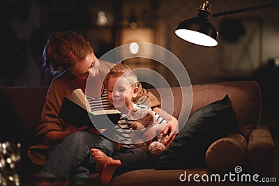 Family before going to bed mother reads to her child son book near a lamp in the evening Stock Photo