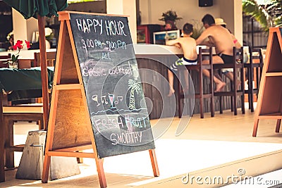 Family during happy hours at tropical beach cafe with signboard during summer beach holidays Stock Photo
