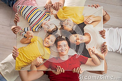 Family holds the same picture of themselves while lying on the floor, smiling Stock Photo