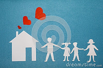 Family and home love concept. Paper house and family on blue textured background. Dad, mom, daughter and son hold hands. Stock Photo