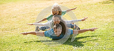 Family leisure time. Family lying on grass in park. Parents giving child piggybacks in park. Stock Photo