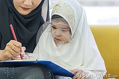 Family lifestyle activity education concept. Daughter mix race girl wear headdress hijab learning write or draw on paper with her Stock Photo