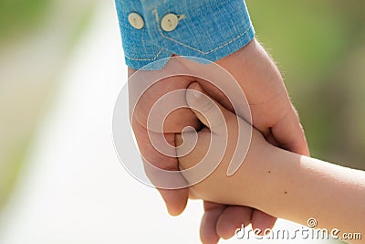 Family. Little child holding hands with his father outdoors, closeup. Family time. Closeup of two touching hands of Stock Photo