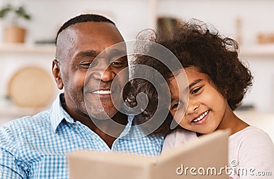 Family lockdown hobbies. African American child listening to her grandfather read bedtime story at home Stock Photo