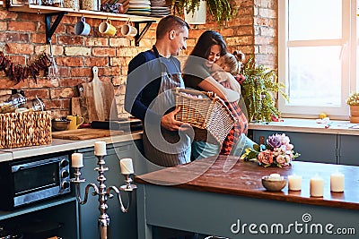 Family in loft style kitchen at morning. Father holds a basket with flowers while mother hugging with her little Stock Photo