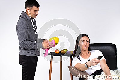 Family. A man is wiping dishes, a woman is watching TV in an armchair. White background. Gender stereotypes Stock Photo