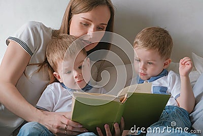 Family mom and two twin brothers toddlers read books laying on the bed. Family reading time. Stock Photo