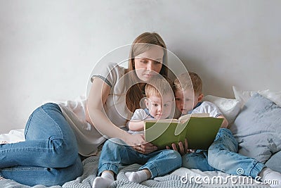 Family mom and two twin brothers toddlers read books laying on the bed. Family reading time. Stock Photo