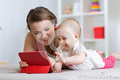 Family - mother and baby with tablet on floor at home. Woman and child girl relaxing at tablet computer. Stock Photo