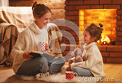 family mother and child reading book on winter evening by fireplace. Stock Photo