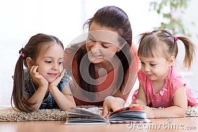 Cute mother and children daughters lie on floor and read book together Stock Photo