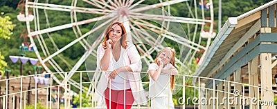 Family. Mother and daughter spend boring time together in an amusement Park. Ferris wheel in the background. Panorama. Concept of Stock Photo