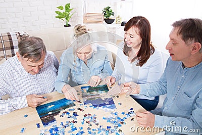 Family play in puzzles at home, elderly couple and middle-aged couple working on a jigsaw puzzle together at home Stock Photo