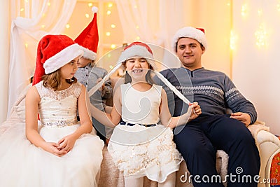 Family portrait - parent and children in home interior decorated with holiday lights and gifts, dressed in santa hat for new year Stock Photo