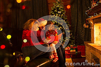 Family read stories at Christmas time sitting on sofa in front of fireplace Stock Photo