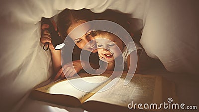 Family reading bedtime. Mom and child reading book with a flashlight under blanket Stock Photo