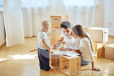 Family reading instruction and assemble furniture together at living room of new apartment pile of moving boxes on Stock Photo