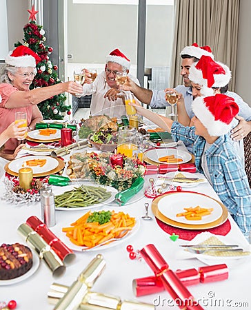 Family in santas hats toasting wine glasses at dining table Stock Photo