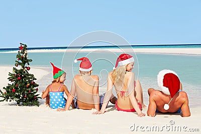 Family Sitting On Beach With Christmas Tree And Hats Stock Photo