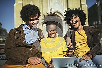Family sitting on bench, relaxing using digital tablet, shopping online Stock Photo