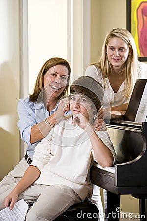 Family sitting on piano bench, mother teasing son Stock Photo