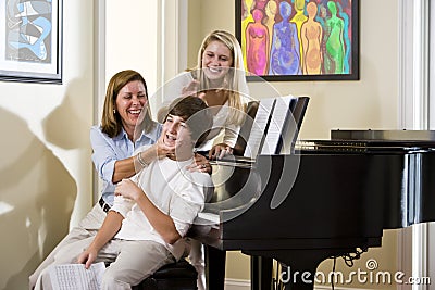 Family sitting on piano bench, mother teasing son Stock Photo