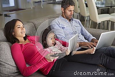 Family On Sofa With Laptop And Digital Tablet Watching TV Stock Photo