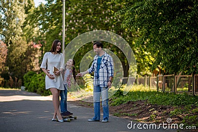 Family Spend Time In The City Park. Father Is Helping Daughter To Ride On The Skateboard In The Park. Stock Photo