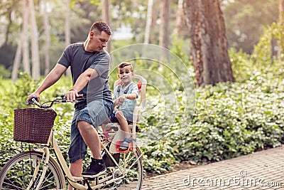 Family sport and healthy lifestyle- father and son riding a bicycle together outdoors in a city park. Stock Photo