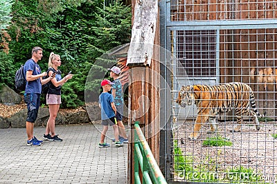 Family standing in zoo and looking at tiger in cage Editorial Stock Photo