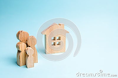 Family stands near a wooden house on a blue background. The concept of affordable housing and mortgages for buying a home Stock Photo