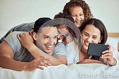 Family taking a selfie with a cellphone in bed. Happy hispanic family taking photos in bed on a smartphone. Parents Stock Photo