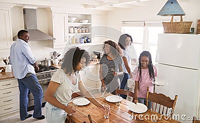 Family With Teenage Daughters Laying Table For Meal In Kitchen Stock Photo