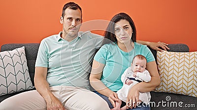 Family of three looking serious sitting on the sofa at home Stock Photo