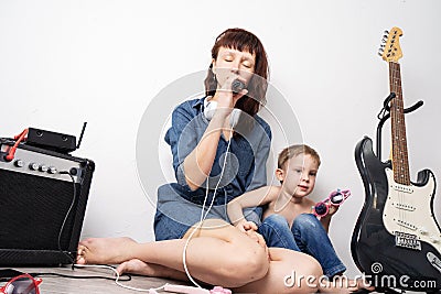 Family time: mother with son staged a home concert and sing with a microphone and an electric guitar. Stock Photo